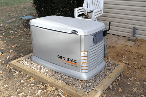 A Generac Guardian Series standby generator, expertly installed by a residential electrician Suffolk County, sits on a gravel platform beside a beige building, with a white plastic chair and scattered leaves nearby.