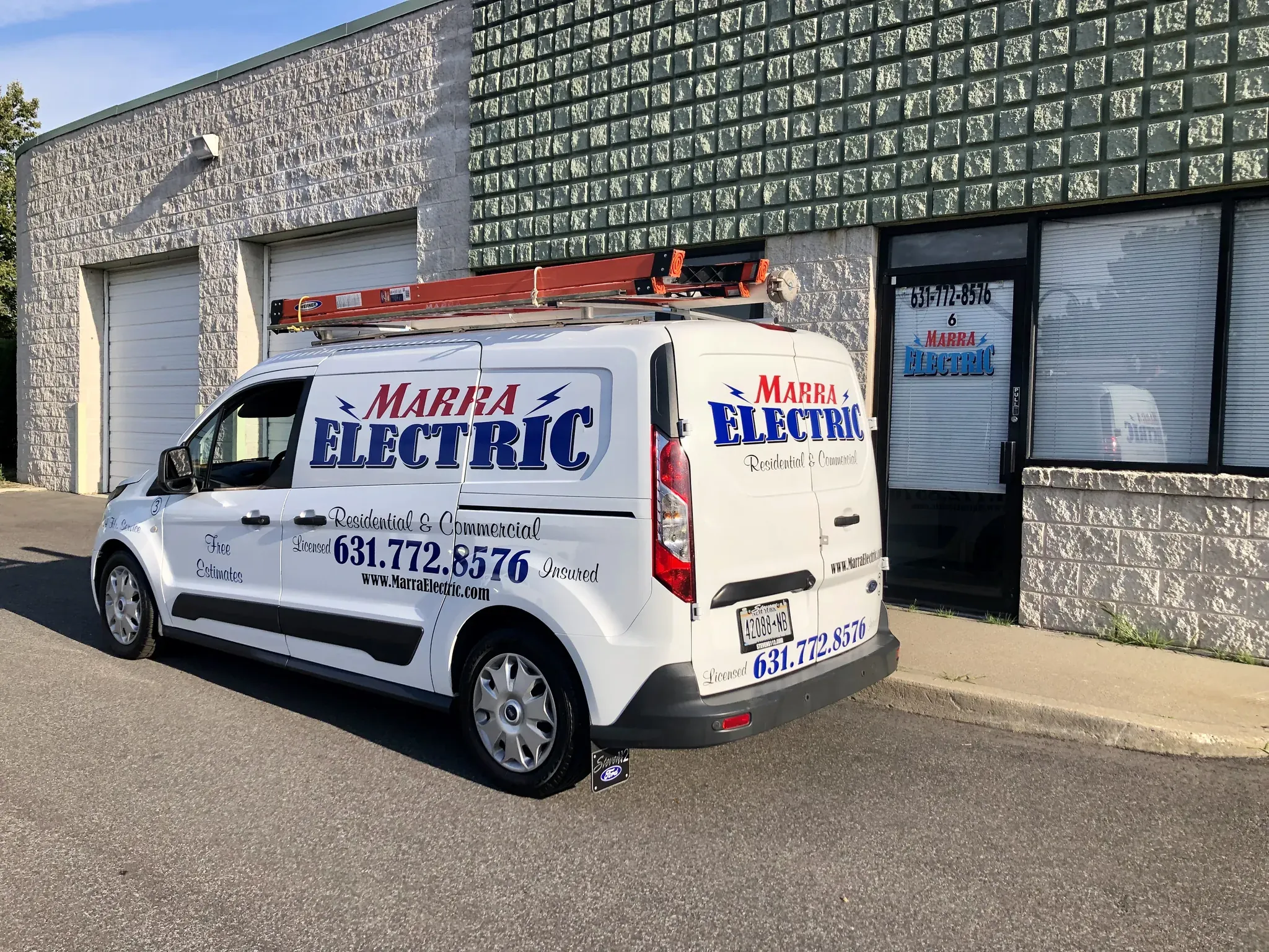 A white Marra Electric van with a ladder on top is parked outside a commercial building. As trusted residential and commercial electricians in Suffolk County, NY, their van displays contact info and advertises expert electrical services.