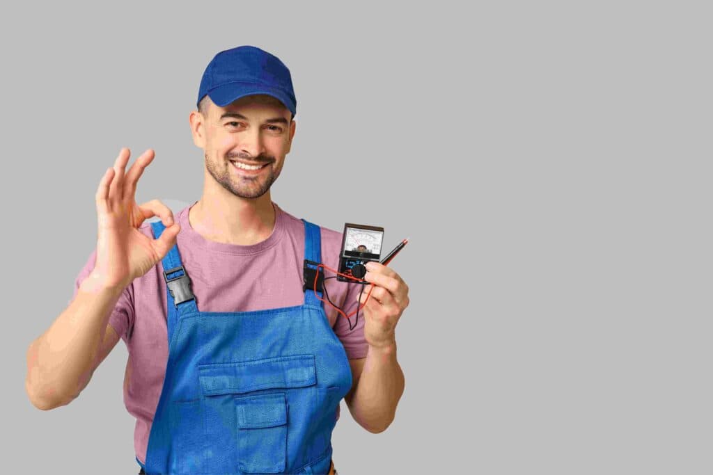 A man in a Suffolk County, NY electrician uniform is captured in a friendly moment, holding an electrical device. He's smiling and giving an "ok" hand gesture with his other hand, showing his confidence and skill.